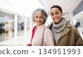 Two smiling middle aged POC women shopping at mall, carrying shopping bags 134951993