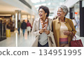 Two smiling middle aged POC women shopping at mall, carrying shopping bags 134951995