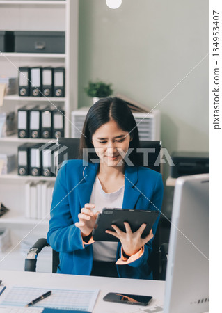 A smiling woman in a lab coat uses a tablet in a bright, modern environment. 134953407