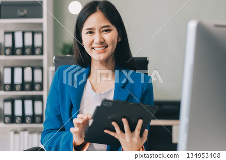A smiling woman in a lab coat uses a tablet in a bright, modern environment. 134953408
