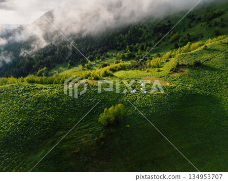 Above view of hiking tents in a mountain valley with forest, mist, and morning sunlight in summer. Above view of hiking tents in a mountain valley with forest, mist, and morning sunlight in summer. 134953707