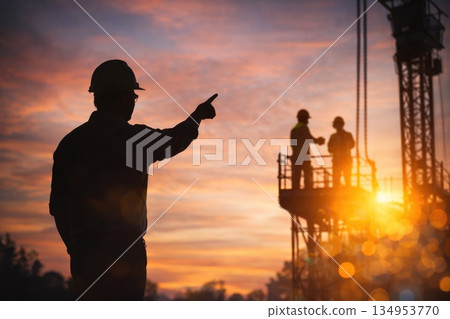 Construction Site Supervisor Pointing Direction at Sunset with Industrial Silhouettes Construction Site Supervisor Pointing Direction at Sunset with Industrial Silhouettes 134953770