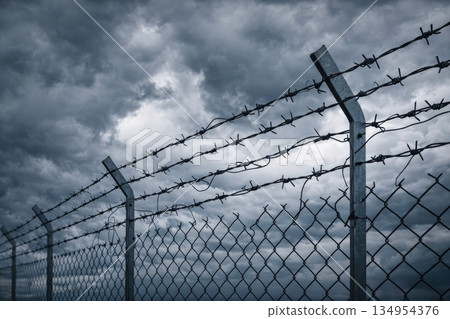 Barbed Wire Fence Under Dark Stormy Sky Representing Restriction, Danger and Security 134954376