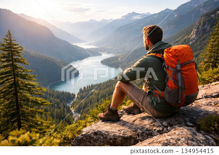 Male backpacker resting on cliff and admiring scenic mountain lake landscape during summer hike Male backpacker resting on cliff and admiring scenic mountain lake landscape during summer hike 134954415