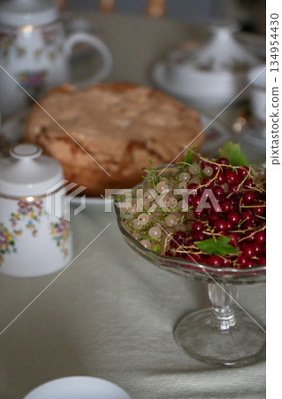 Glass bowl with red and white currants stands on a tea table with homemade apple charlotte and floral teaware softly blurred in the background Glass bowl with red and white currants stands on a tea table with homemade apple charlotte and floral teaware softly blurred in the background 134954430