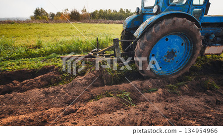 Blue tractor plowing the field in autumn. 134954966