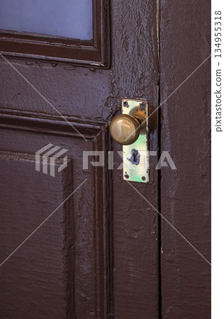 Old brown wooden door with grill, brass doorknob or handle in lock position. 134955318