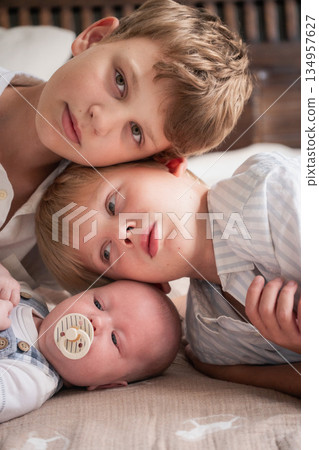 Three brothers lie close together, their heads gently touching, creating a warm and intimate family portrait Three brothers lie close together, their heads gently touching, creating a warm and intimate family portrait 134957627