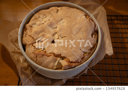 Freshly baked apple pie with golden crust cools in a baking dish on parchment paper, warm tones, cozy homemade baking atmosphere Freshly baked apple pie with golden crust cools in a baking dish on parchment paper, warm tones, cozy homemade baking atmosphere 134957628