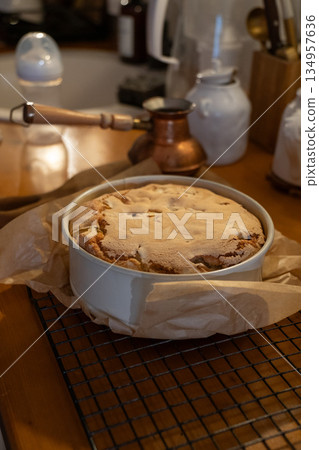 Freshly baked apple pie with golden crust cools in a baking dish on parchment paper, warm tones, cozy homemade baking atmosphere 134957636