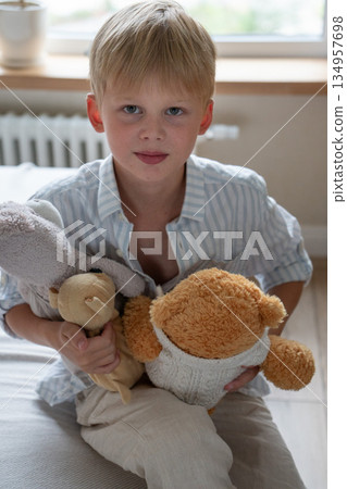Young boy hugs soft teddy bears at home, portrait with gentle daylight, neutral colors, calm and comforting childhood moment 134957698