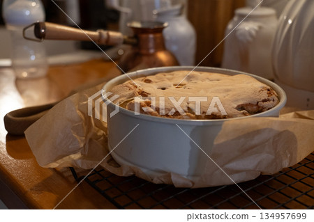 Freshly baked apple pie cools in a round baking dish on parchment paper, warm kitchen light, rustic textures, cozy homemade baking mood 134957699