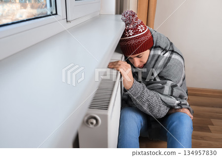 Frozen man in winter hat and blanket leaning on central heating radiator to warm up at home. High quality photo Frozen man in winter hat and blanket leaning on central heating radiator to warm up at home. High quality photo 134957830