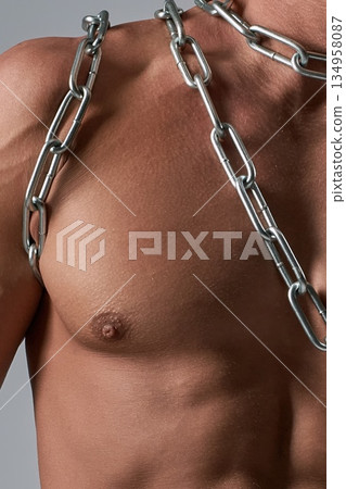 Close-up of a powerful male chest and muscular torso wrapped in a silver chain. Close-up of a powerful male chest and muscular torso wrapped in a silver chain. 134958087