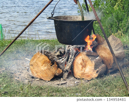 A large pot is on a tripod over a fire 134958481