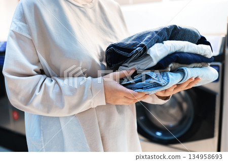 Woman holding stack of clean folded clothes in laundry room. Person with pile of fresh laundry near washing machine. High quality photo Woman holding stack of clean folded clothes in laundry room. Person with pile of fresh laundry near washing machine. High quality photo 134958693
