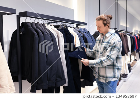 man choosing clothes in fashion store. Male customer inspecting trousers on rack at shopping mall. High quality photo man choosing clothes in fashion store. Male customer inspecting trousers on rack at shopping mall. High quality photo 134958697