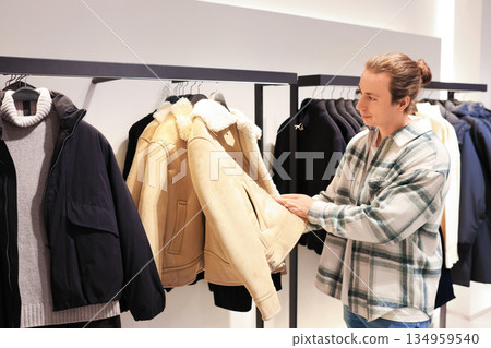 man browsing winter clothes in a fashion store, examining a beige shearling jacket on a rack. High quality photo man browsing winter clothes in a fashion store, examining a beige shearling jacket on a rack. High quality photo 134959540
