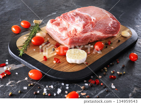 Fresh raw pork meat on a wooden board with rosemary, garlic, tomatoes, and spices on a dark marble background. High quality photo Fresh raw pork meat on a wooden board with rosemary, garlic, tomatoes, and spices on a dark marble background. High quality photo 134959543