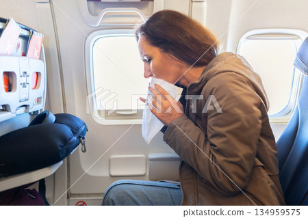 Adult caucasian woman feeling sick inside airplane cabin holding paper bag Adult caucasian woman feeling sick inside airplane cabin holding paper bag 134959575