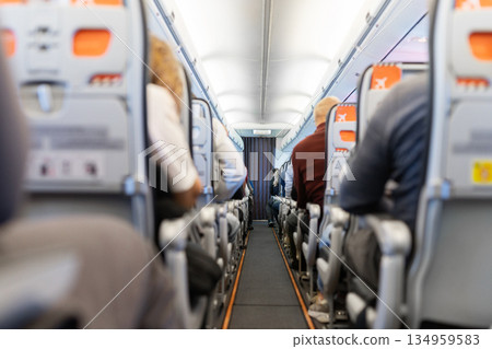 View down airplane aisle with seated passengers during flight. Commercial air travel View down airplane aisle with seated passengers during flight. Commercial air travel 134959583