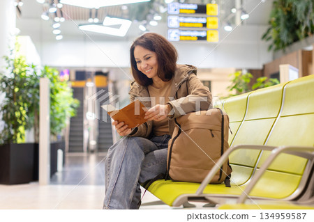 Smiling caucasian woman sitting at airport terminal reading passport documents 134959587