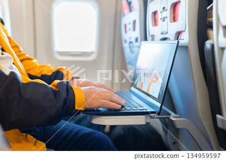 Closeup of adult man using laptop on airplane tray table during flight Closeup of adult man using laptop on airplane tray table during flight 134959597