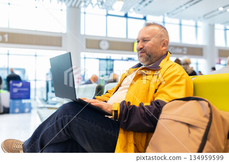 Adult caucasian man working on laptop while waiting at airport terminal Adult caucasian man working on laptop while waiting at airport terminal 134959599