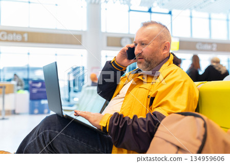 Business traveler talking on smartphone while using laptop at airport gate 134959606