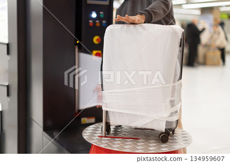 Wrapped suitcase being prepared for flight at airport luggage service area 134959607