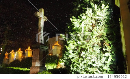 On Christmas New Year Eve, during snowstorm and blizzard, religious Orthodox cross stands firm in churchyard. A thuja tree, covered in snow, sways in the winter wind. A symbol of faith and fortitude. On Christmas New Year Eve, during snowstorm and blizzard, religious Orthodox cross stands firm in churchyard. A thuja tree, covered in snow, sways in the winter wind. A symbol of faith and fortitude. 134959912