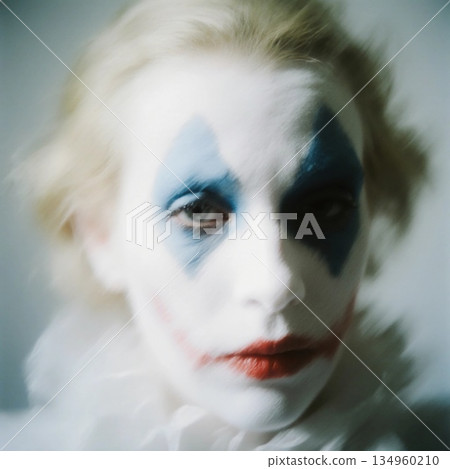 The clown harlequin with pale skin sits quietly, his blue and red face paint accentuating his sadness. Soft lighting creates a moody atmosphere, highlighting his emotions Generative AI 134960210