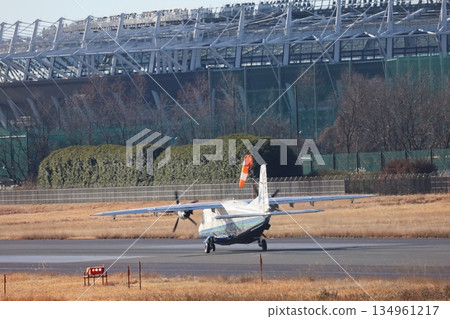 A small propeller passenger plane takes off from the runway in front of Ajinomoto Stadium toward the island. A small propeller passenger plane takes off from the runway in front of Ajinomoto Stadium toward the island. 134961217