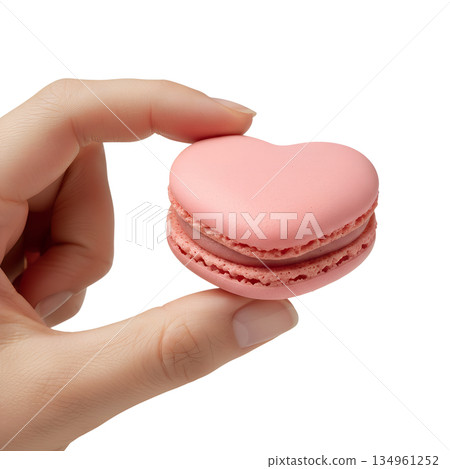 Delicate pink heart-shaped french macaron held carefully in a hand, representing elegant desserts, valentine's gifts, and patisserie art 134961252