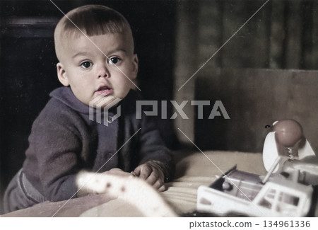 Vintage portrait of little boy playing with toy cars in living room. Funny photo of cute boy. Retro photo from 1970s. 134961336