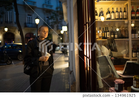 Woman holding coffee cup on nighttime city street Woman holding coffee cup on nighttime city street 134961925