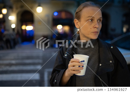 Woman holding coffee cup on evening street Woman holding coffee cup on evening street 134961927