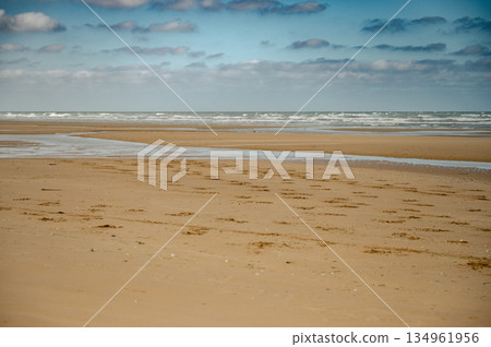 A wide view of Omaha Beach's peaceful shoreline in Normandy, France. Once a historic World War II landing site, the beach now offers a calm and reflective coastal landscape. 134961956