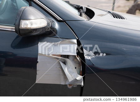 Side view of damaged blue car with taped mirror and dented panel 134961986