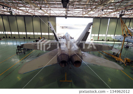 Rear top view of twin engine fighter jet in maintenance hangar 134962012