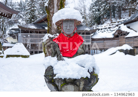 Snow-covered Jizo statue and red apron | A Japanese religious scene at a temple in winter 134962963