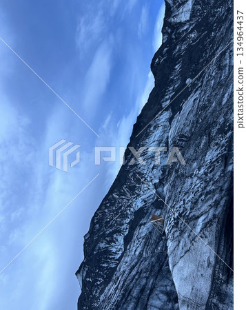 Earth cave tour of Mýrdalsjökull glacier in Iceland, black ice mountains, blue sky and clouds. Earth cave tour of Mýrdalsjökull glacier in Iceland, black ice mountains, blue sky and clouds. 134964437