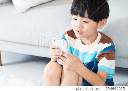 Elementary school boy playing with smartphone in the living room Elementary school boy playing with smartphone in the living room 134964925