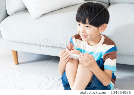 Elementary school boy playing with smartphone in the living room Elementary school boy playing with smartphone in the living room 134964926