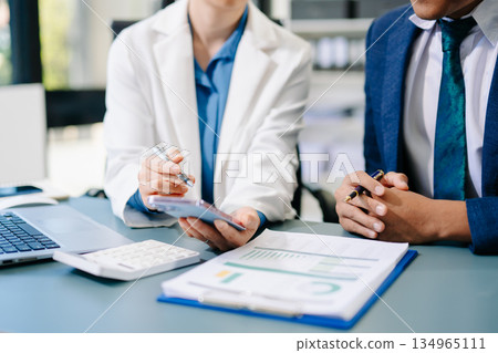 Professional businesspeople analyzing data, discussing strategy, and collaborating on financial reports in a modern corporate office setting. 134965111