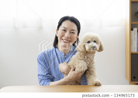 A woman in her 50s smiling and looking at the camera while holding a dog 134965173