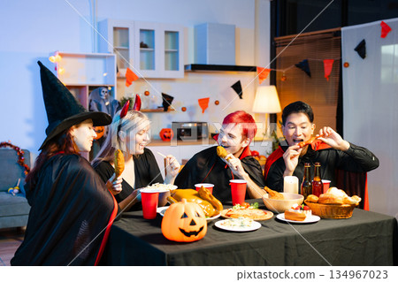 Friends in spooky Halloween costumes enjoy drinks and food at a festive indoor party with pumpkins, red cups, and laughter. Friends in spooky Halloween costumes enjoy drinks and food at a festive indoor party with pumpkins, red cups, and laughter. 134967023