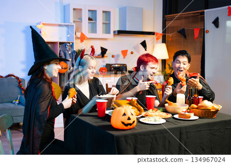 Friends in spooky Halloween costumes enjoy drinks and food at a festive indoor party with pumpkins, red cups, and laughter. Friends in spooky Halloween costumes enjoy drinks and food at a festive indoor party with pumpkins, red cups, and laughter. 134967024