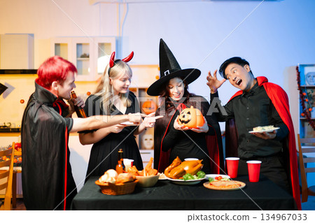 Group of young friends in Halloween costumes enjoy food and drinks at a cozy indoor party. with fun, spooky vibes, red cups, and pumpkin decor. 134967033
