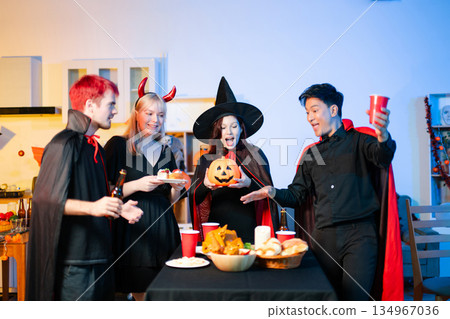 Group of young friends in Halloween costumes enjoy food and drinks at a cozy indoor party. with fun, spooky vibes, red cups, and pumpkin decor. Group of young friends in Halloween costumes enjoy food and drinks at a cozy indoor party. with fun, spooky vibes, red cups, and pumpkin decor. 134967036